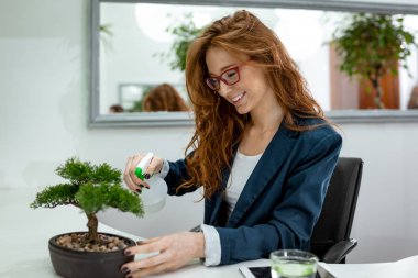 Bonsai ağacı ve gülümseyen su püskürtme genç iş kadını 