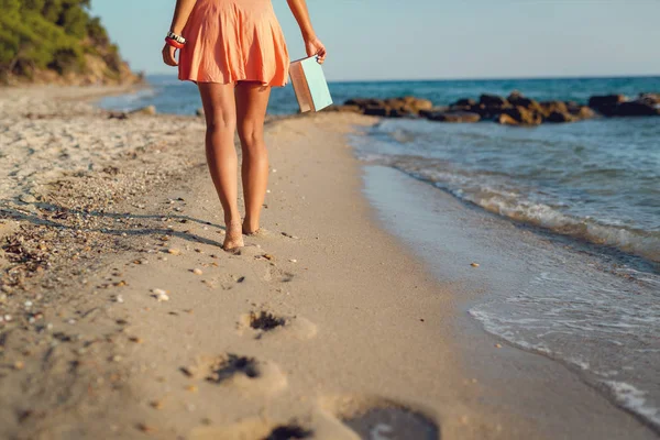 Γυναίκα Στην Πορτοκαλί Φόρεμα Κρατώντας Βιβλίο Και Περπάτημα Στην Παραλία — Φωτογραφία Αρχείου
