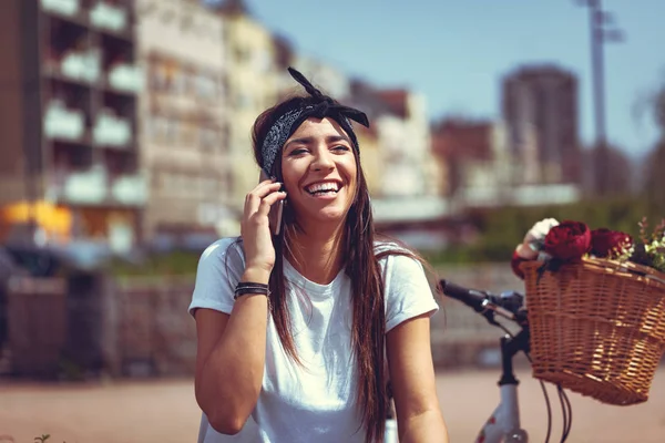 young woman with bike with flower basket using smartphone and drinking coffee