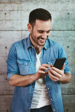 Beton duvar önünde Smartphone kullanarak genç başarılı girişimci