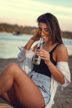 Gün batımında sahilde bira içme hasır şapka olan kadın