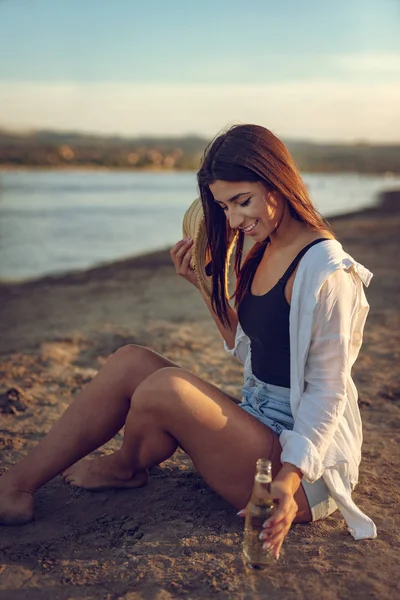 Gün batımında sahilde bira içme hasır şapka olan kadın