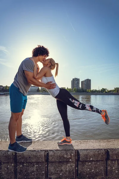 Genç çift dinlenme ve gün batımında nehir tarafından başarılı eğitim sonrası öpüşme