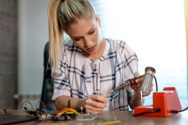Genç kadın teknisyeni havya tarafından elektronik donatımın tamiri üzerinde duruldu