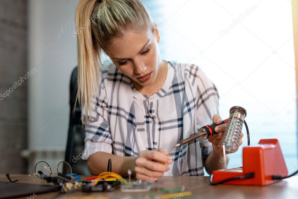 Young woman technician focused on repairing of electronic equipment by soldering iron