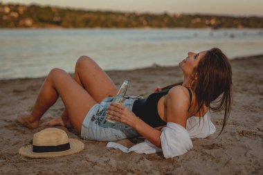 Gün batımında sahilde bira içme hasır şapka olan kadın