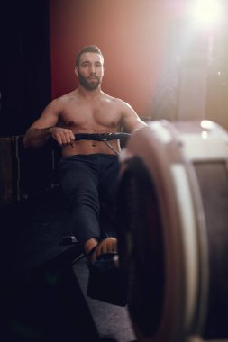 Genç kaslı adam kürek makine spor salonunda çekerek