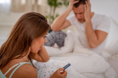 Yatağın üstüne oturan ve gebelik testi seyir endişeli genç kadın