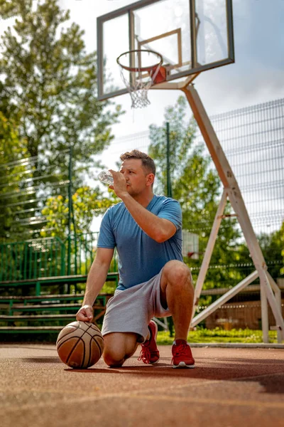 年轻街头篮球运动员玩和喝水后在球场上休息 — 图库照片