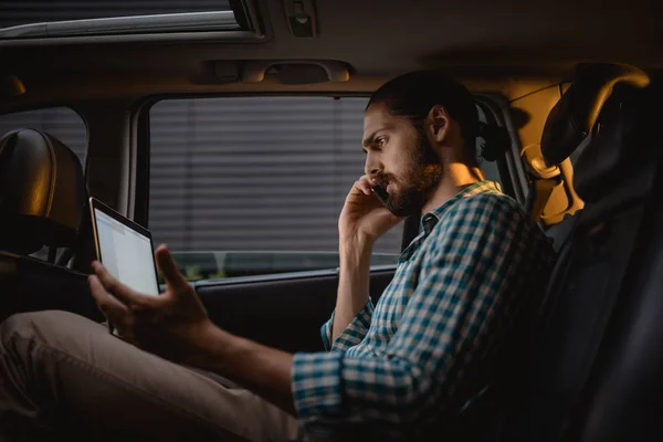 スマート フォンで話していると 車の後部座席に座りながらノート パソコンを見て自信を持ってきしゃ — ストック写真