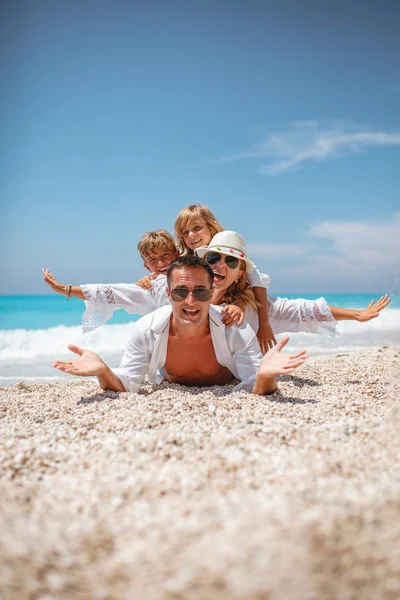 ビーチで砂の上に横たわっている間楽しい時を過す小さな子供たちと幸せな若い家族 — ストック写真