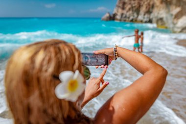 Fotoğrafta oğulları tropik sahilde dalgalar deniz içinde smartphone kadınla
