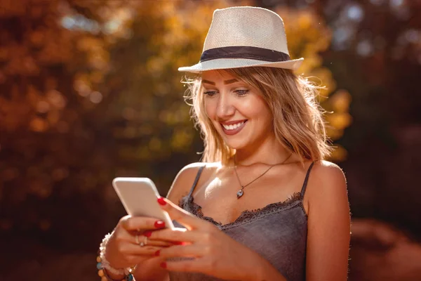 Uśmiechnięta Młoda Kobieta Kapeluszu Przy Użyciu Smartfona Jesienny Park — Zdjęcie stockowe