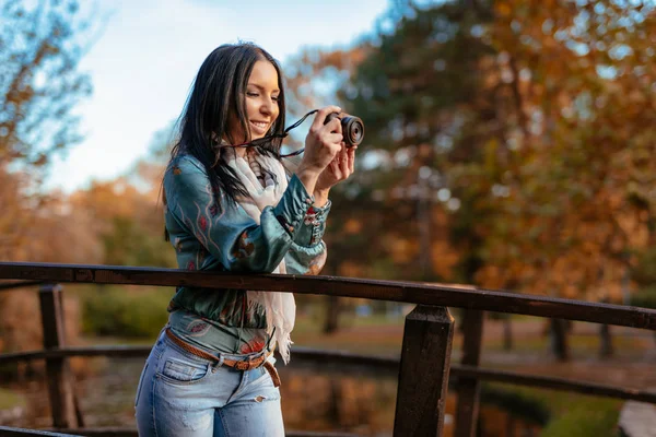 Woman holding professional digital camera and taking photo in autumn city park
