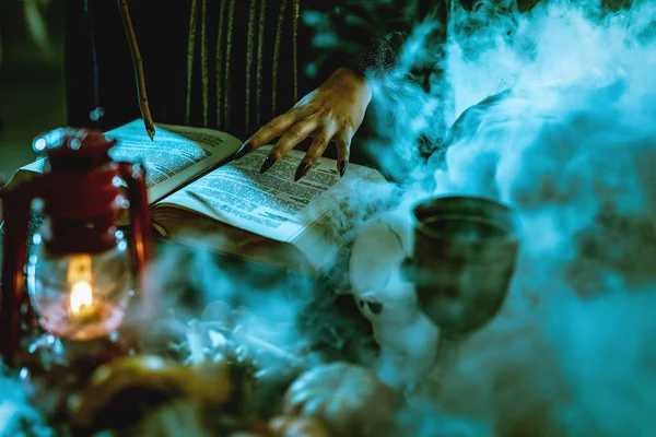 接近看巫婆手与针对性的黑钉子在黑烟的魔术食谱书 — 图库照片