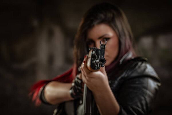 Женщина, стоящая в положении прицеливания и глядя сквозь прицел автоматической винтовки
