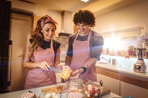 Cute couple is putting vegetables in a jar and smiling while making pickle in kitchen at home