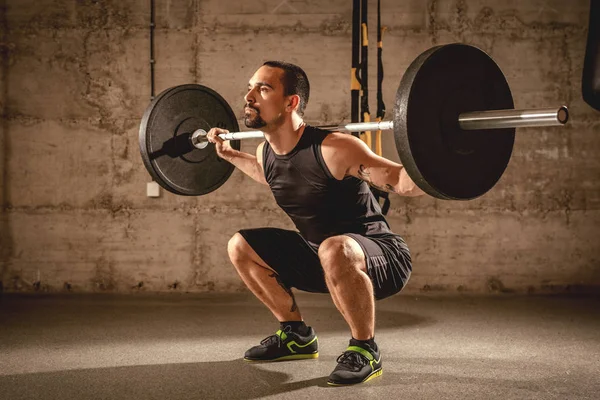 英俊的年轻肌肉发达的男子在健身房用杠铃做蹲运动 — 图库照片