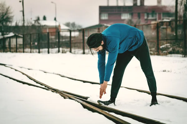 Active young man stretching and doing exercises in old factory place among old railroad