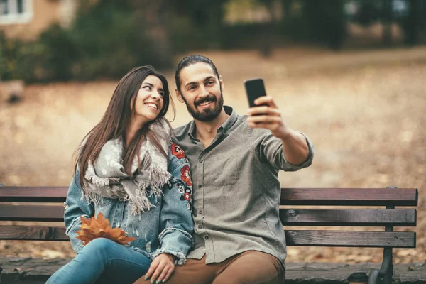 Χαμογελαστά Ζευγάρι Κάθεται Στον Πάγκο Και Χρησιμοποιώντας Smartphone — Φωτογραφία Αρχείου