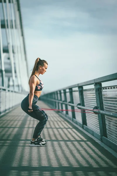肌肉发达的年轻女子在桥上用弹性橡皮筋进行强壮的健身训练 — 图库照片