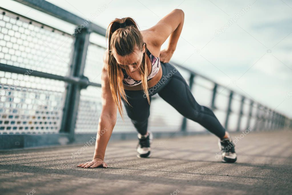 Young female runner doing push-ups exercise on river bridge