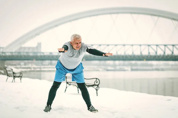 Aktywne Starszy Mężczyzna Rozciągający Się Nad Rzeką Podczas Treningu Zimowe — Zdjęcie stockowe