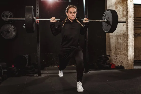 Young muscular woman doing lunges exercise with barbell at gym