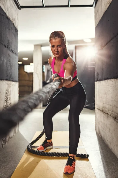 Young muscular woman doing exercise pulling rope at gym