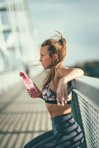 Young fitness woman resting after hard training by river bridge