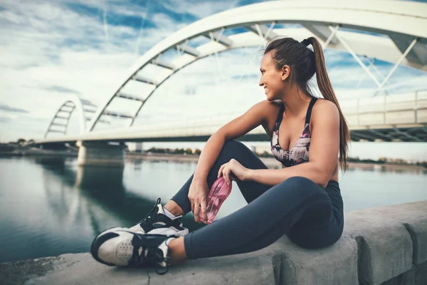 Young fitness woman resting after hard training by river bridge