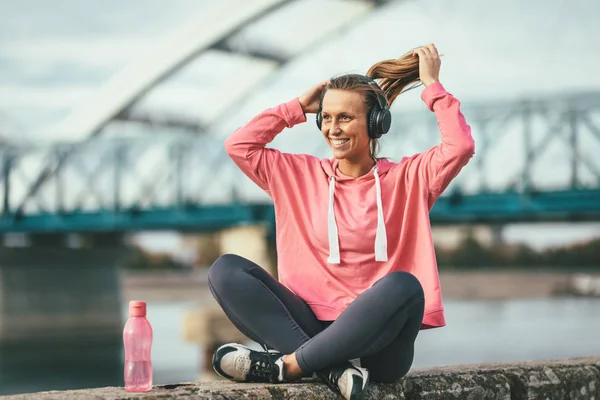 Young fitness woman resting after hard training by river bridge