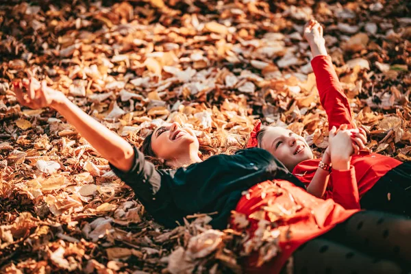 young mother with daughter lying down on golden yellow leaves in forest