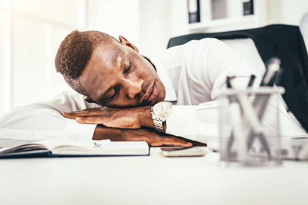 Tired African businessman napping on desk next to documents in office