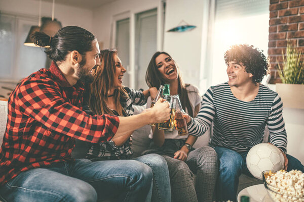 Group of cheerful friends watching football game with beer at home 