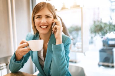 Genç gülümseyen iş kadını smartphone kullanarak kafede kahve molası 