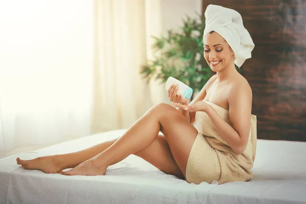 young woman applying body lotion during skin care treatment at spa