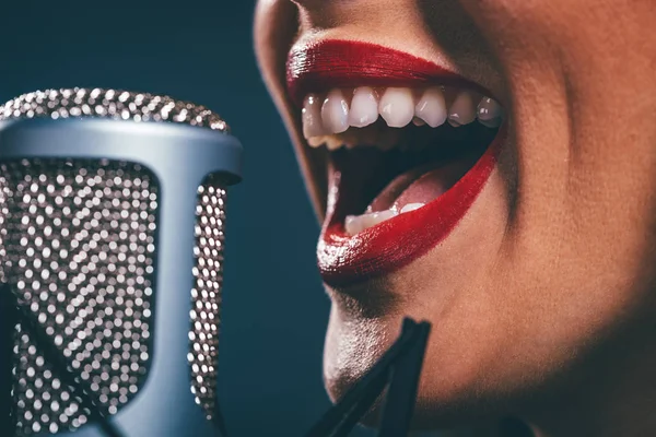 Close view of female open mouth with red lipstick singing on microphone