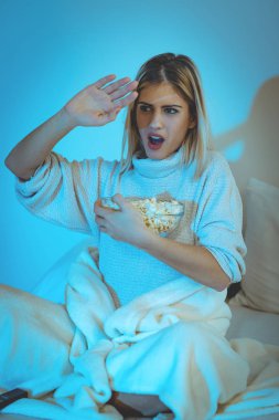 Genç kadın yatakta patlamış mısır ile korku filmi izlerken