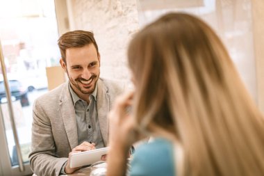 Kafede oturan ve dijital tablet üzerinde çalışan iş adamları gülümseyen iki güzel genç