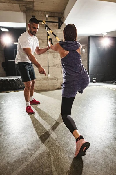 Young muscular woman doing hard workout with personal trainer at garage gym