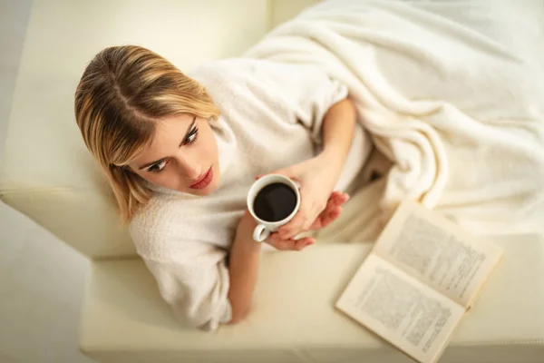 Mujer Joven Bebiendo Café Leyendo Libro Sofá —  Fotos de Stock