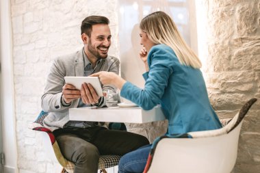 İki güzel genç gülümseyen insanlar kafede oturan ve dijital tablet üzerinde çalışan.