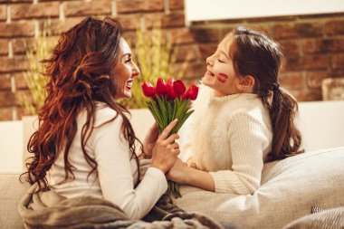 taze buket tutarak ve kızı için öpücük vererek büyüleyici genç anne 