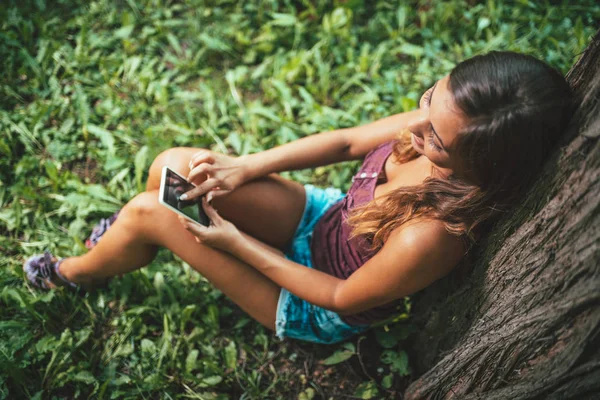 Sonriente Mujer Moderna Mensajes Texto Teléfono Inteligente Sentado Bajo Árbol — Foto de Stock