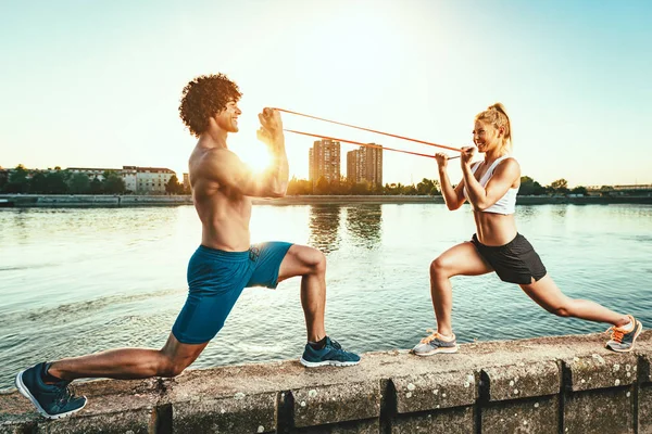年轻的健身夫妇在日落时用河带橡皮筋锻炼身体 — 图库照片