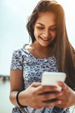 nehir kıyısındaki Smartphone kullanan genç gülümseyen kadın 