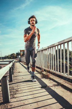 Müzik dinleme ve köprüde koşu kulaklık ile genç adam 