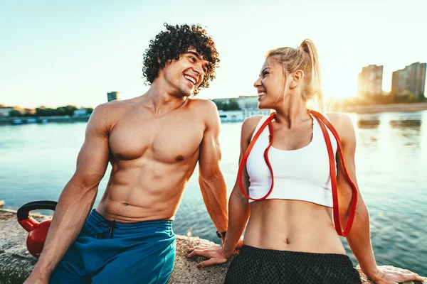 Young fitness couple resting after hard training by river at sunset drinking water