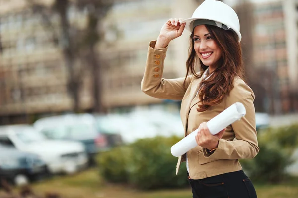 Portrait of young engineer woman with white helmet holding blueprints